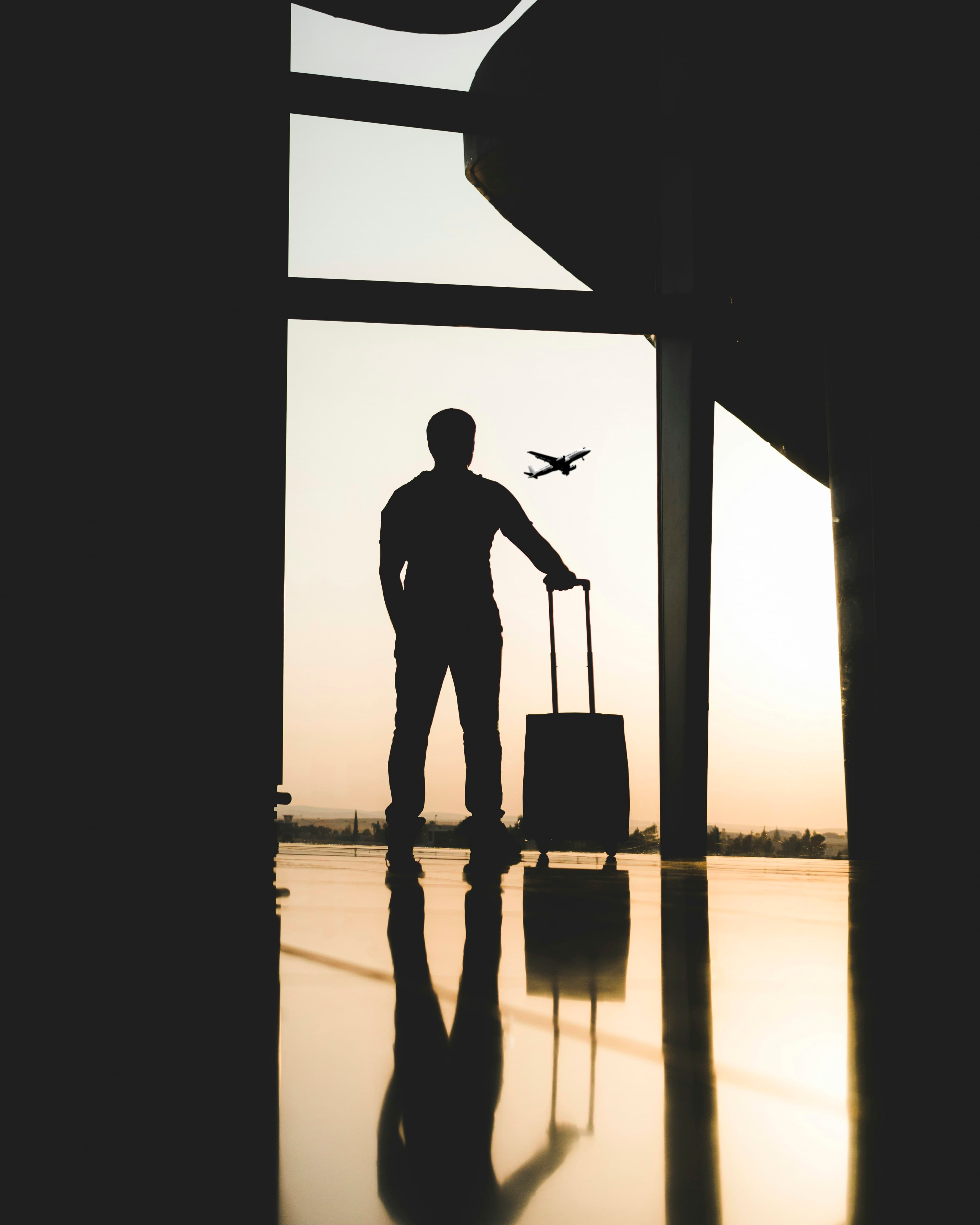 Traveller with a suitcase at an airport window as a plane takes off